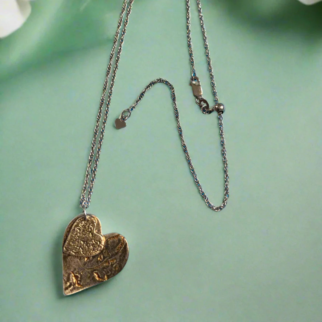 Heart-shaped pendant necklace with oxidized finish on a green surface