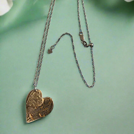 Heart-shaped pendant necklace with oxidized finish on a green  surface