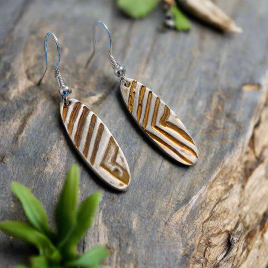 Pair of feather-shaped earrings with brown and silver pattern on a stone surface.