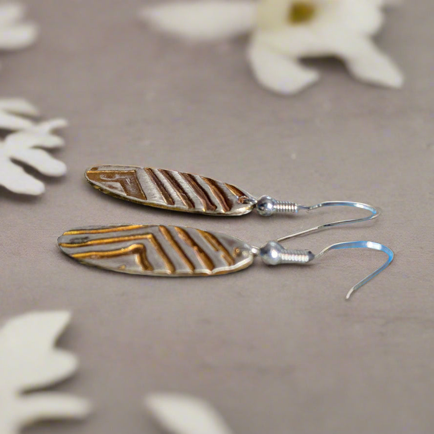 Pair of long oval shaped earrings on a textured stone surface with a blue background
