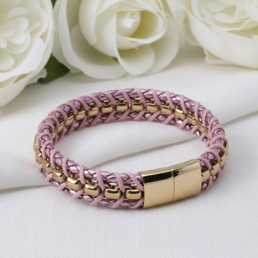Pink braided bracelet with gold accents on a white surface with white roses in the background