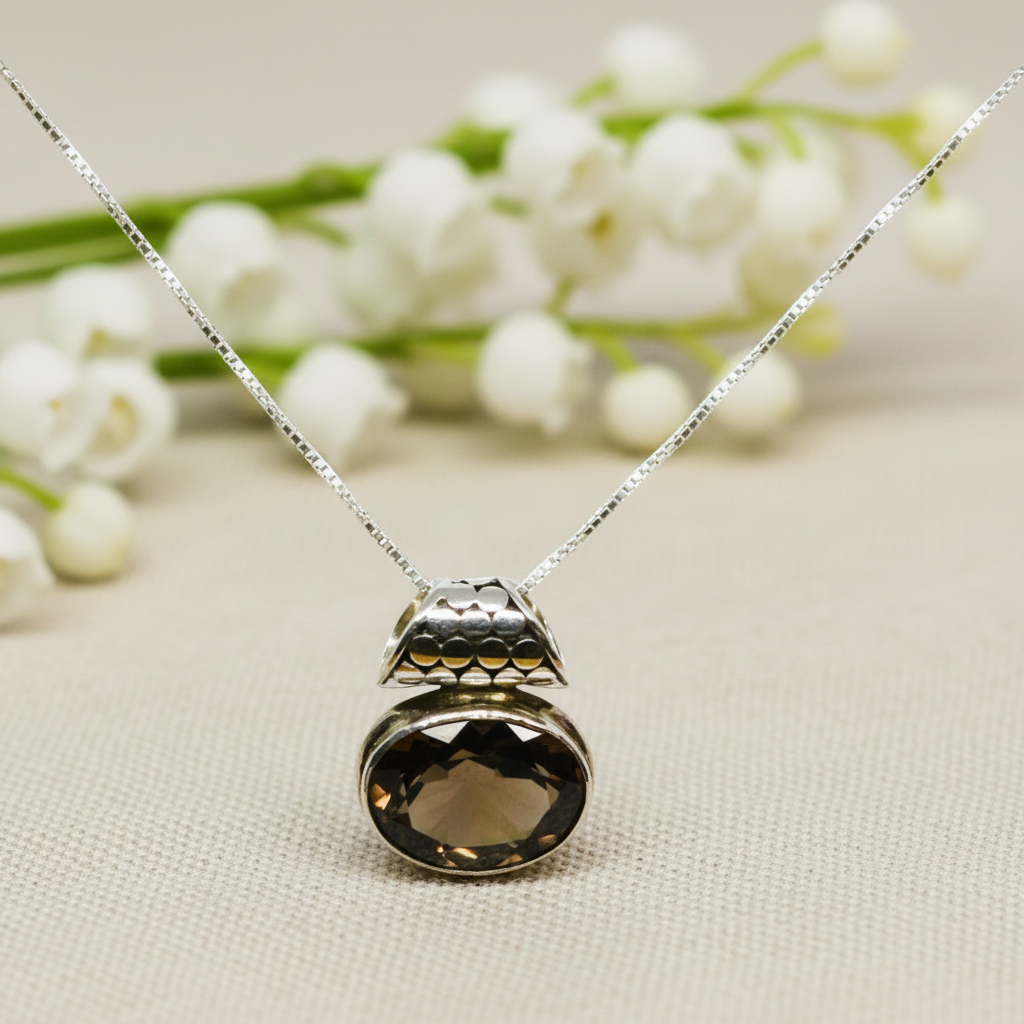 A silver pendant with a smoky topaz gemstone set in a fine chain, displayed against a floral background.
