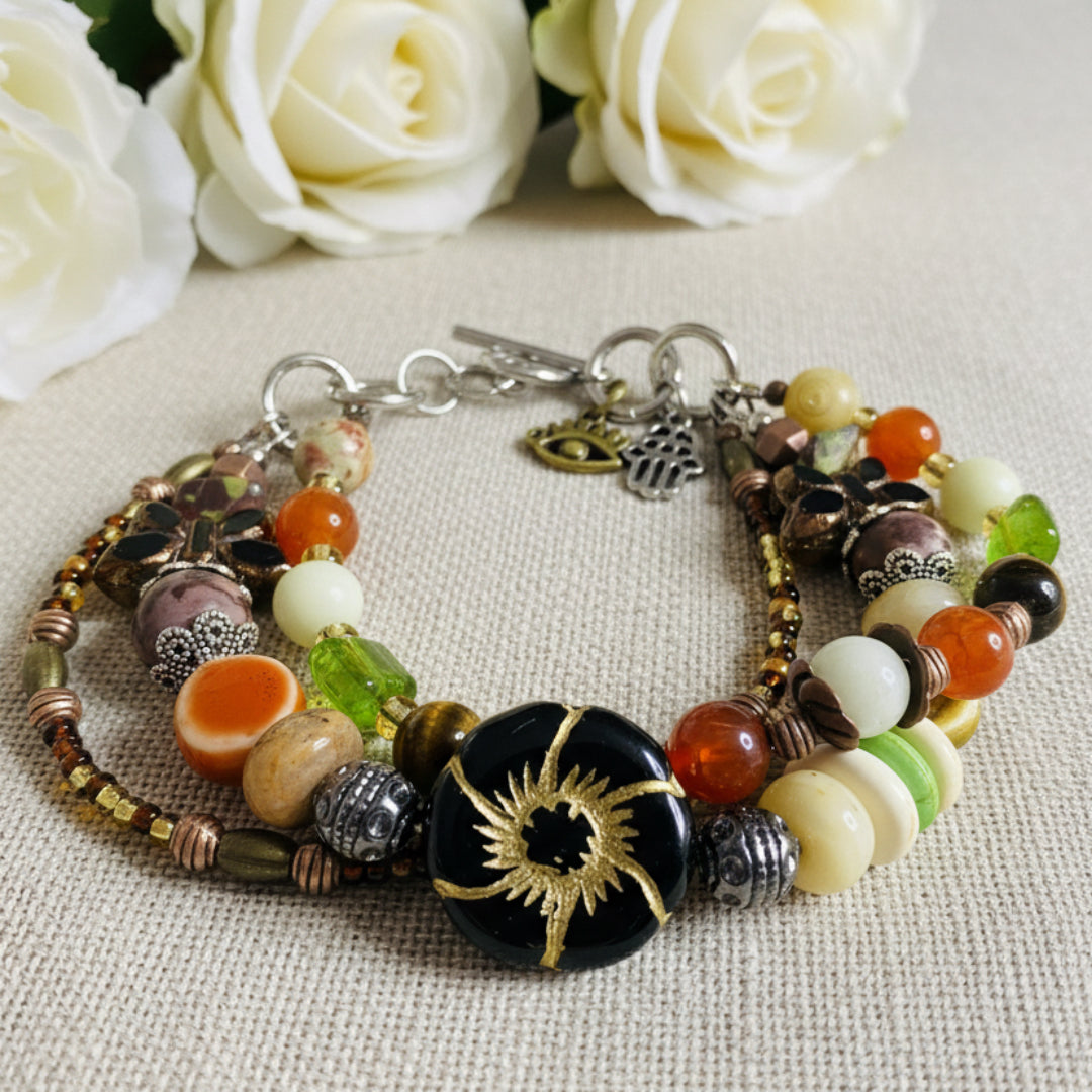 Multicolored beaded bracelet with charms on a textured beige linen background with soft floral accents.