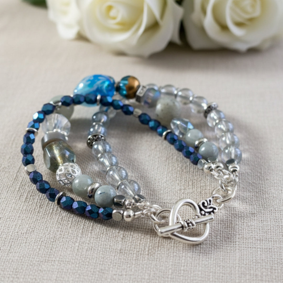 Beaded bracelet in shades of blue and grey with lamp work beads and AB glass.  Silver toggle heart shape fastener.